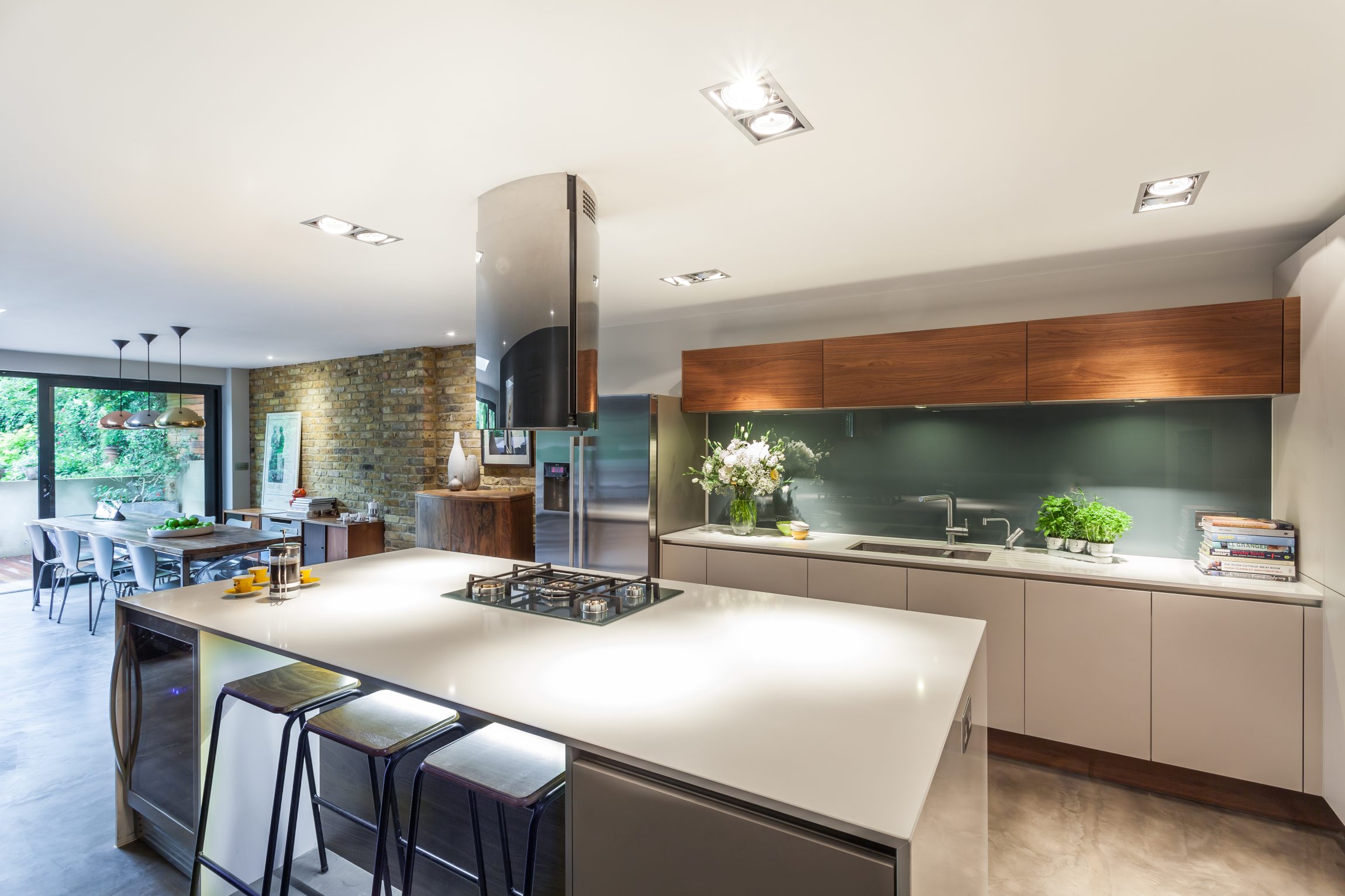 Contemporary open-plan kitchen with painted glass splashback, quartz island, walnut cabinets and microcement flooring—designed by Casey & Fox.